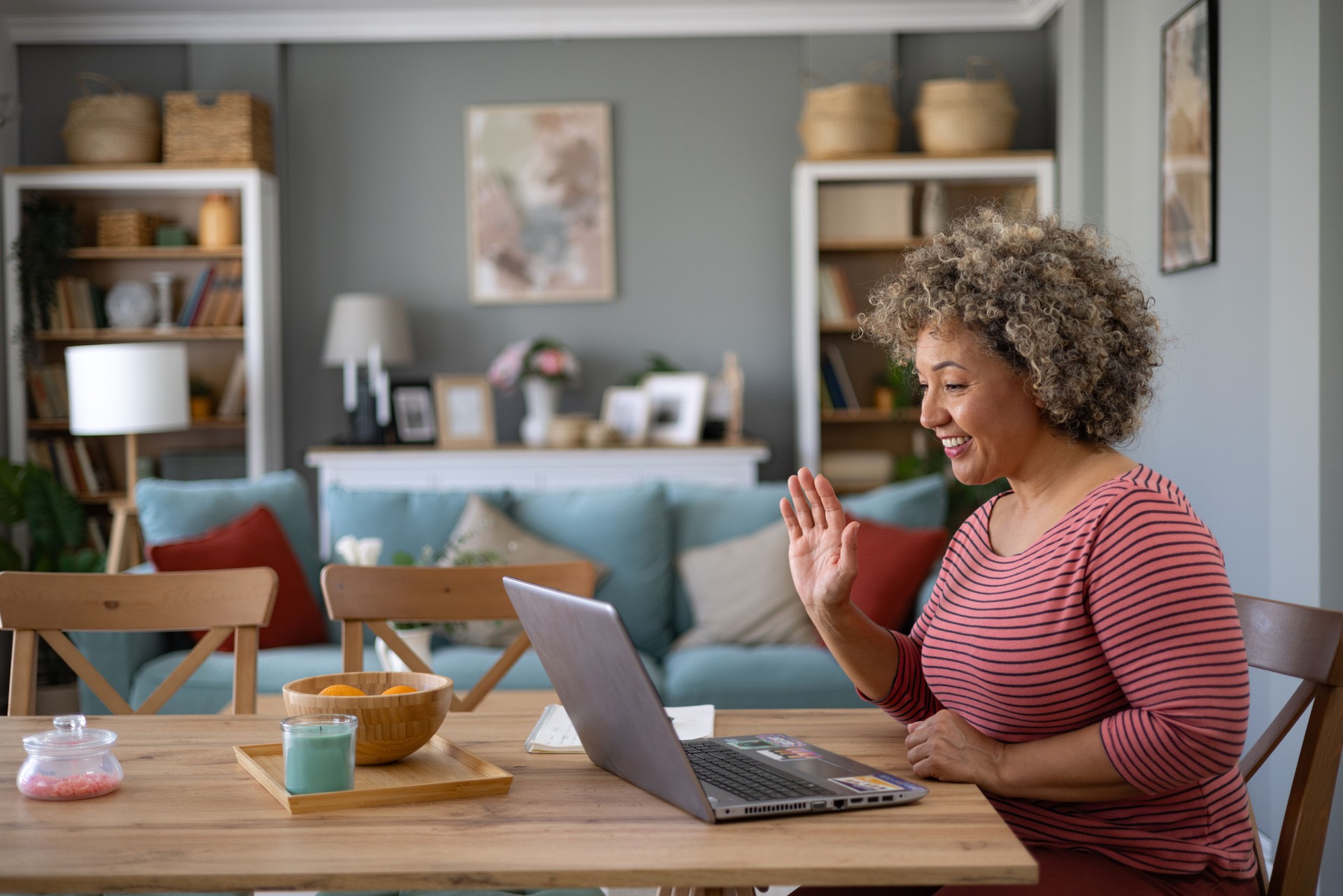 Happy woman greeting someone during video call over laptop at home office.